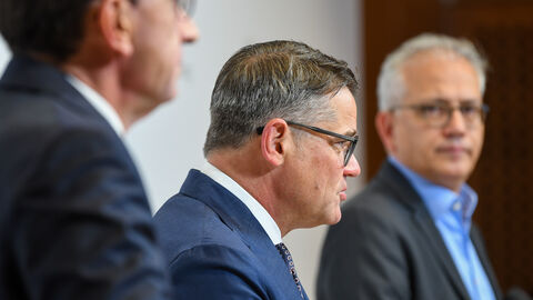 Ministerpräsident Boris Rhein ist im Fokus des Bildes. Wirtschaftsminister Tarek Al-Wazir schaut ihn an. Zu seiner Linken steht FInanzminister Michael Boddenberg.