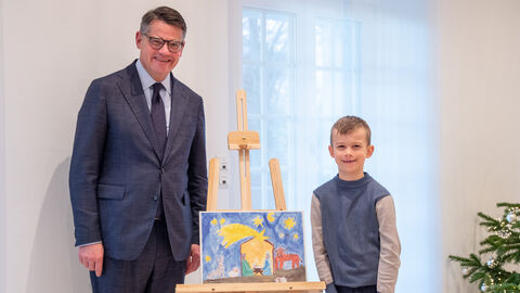 Der Ministerpräsident und der siebenjährige Richard stehen neben dem gemalten Siegerbild und lachen in die Kamera