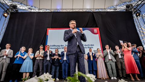 Ministerpräsident Boris Rhein steht auf einer Bühne und spricht zum Publikum. 