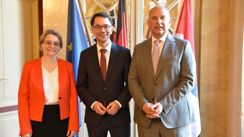 Tanja Eichner, Christian Heinz und Roman Poseck stehen nebeneinander aufgereiht vor Flaggen und schauen in die Kamera.