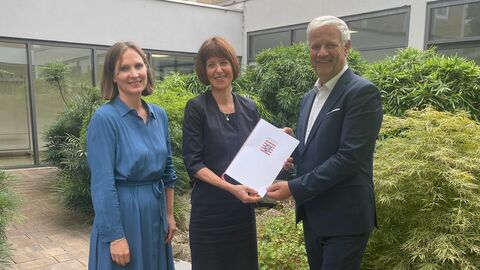 Miriam Zeleke, Sozialministerin Heike Hofmann und Thomas Domnick stehen nebeneinander und halten den Bescheid zur Förderung in der Hand.