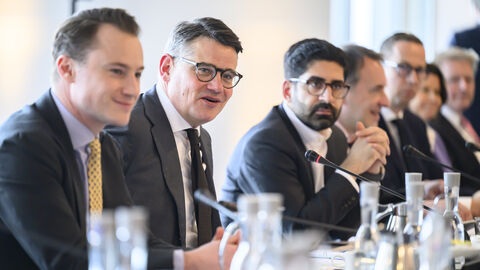 Mehrere Personen sitzen nebeneinander an einem Tisch.