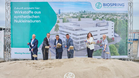 Sechs Personen stehen nebeneinander vor einem Sandhaufen. Sie schütten gerade mit der Schaufel Sand auf den Haufen.